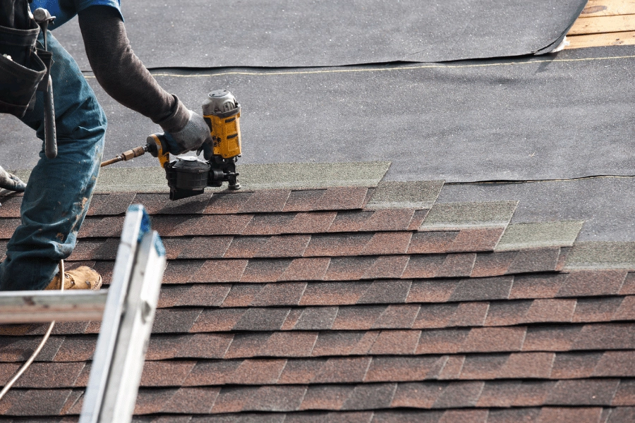 worker standing on a ladder and repairing a roof on a home